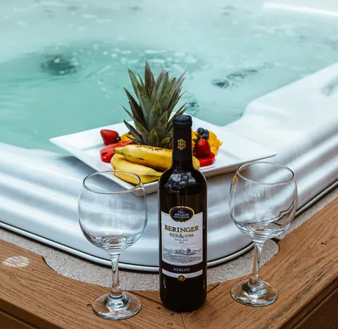 A bottle of wine, two glasses and a fruit platter beside the hot tub