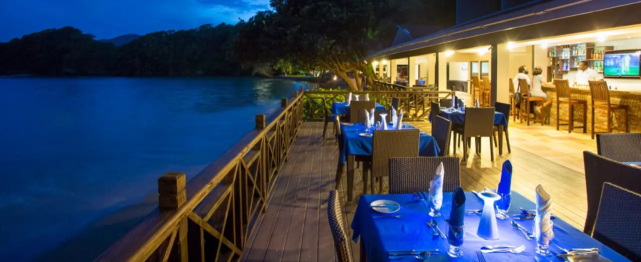 AQUA's deck at dusk, with tables set in blue beside the water and the bar lit up