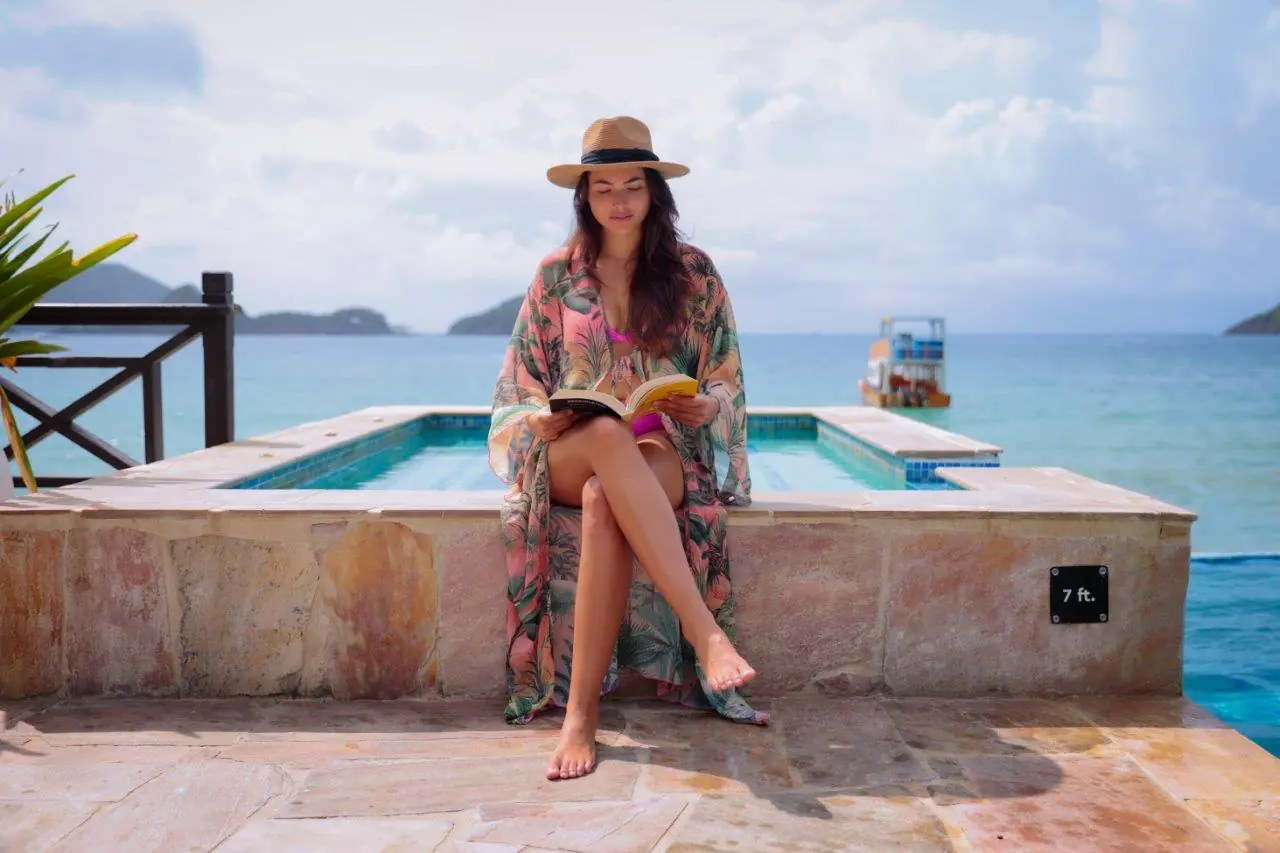A guest reading on the edge of the infinity pool, with the sea and islands behind