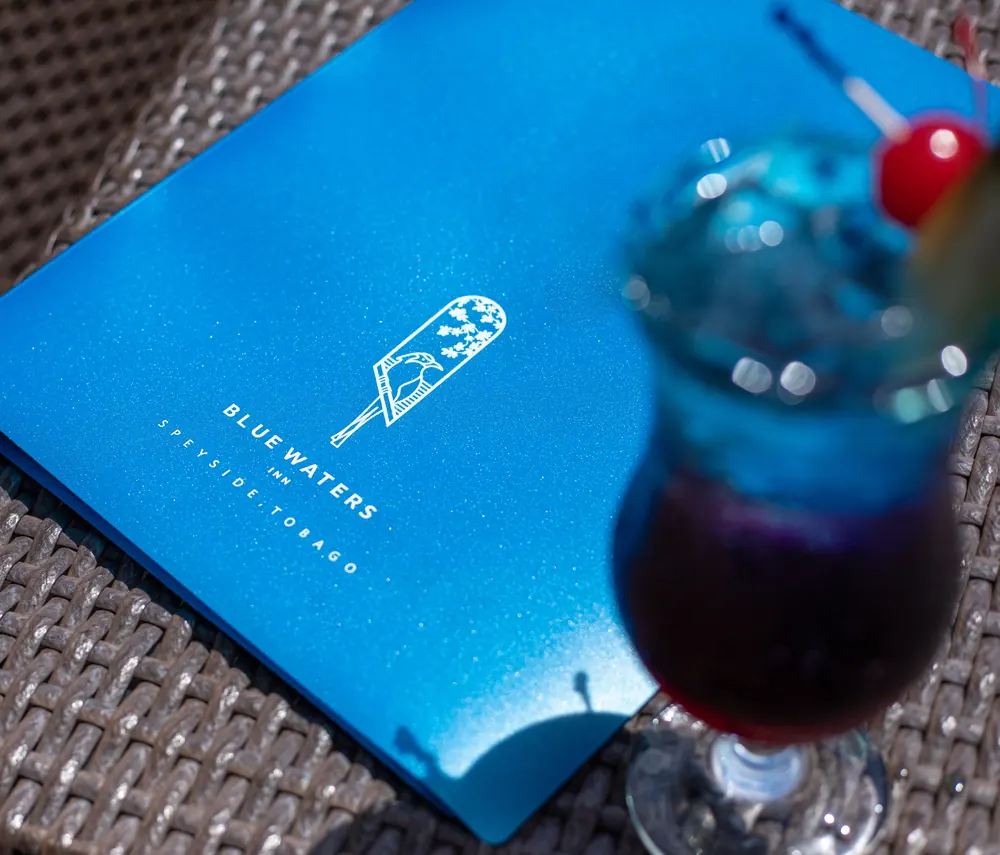 A blue cocktail with a cherry beside a Blue Waters Inn menu