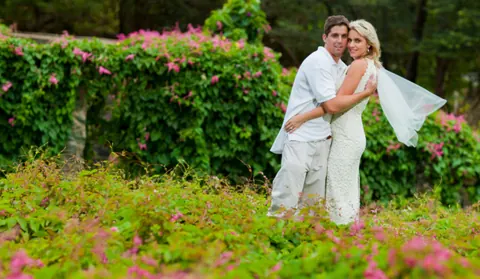 A bride and groom embracing in a garden of pink bougainvillea
